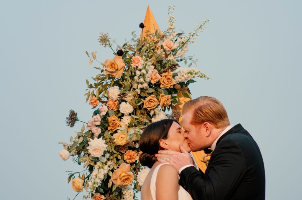 Couple kissing at ceremony arch florals by Fire & Flora The Georgian Peaks